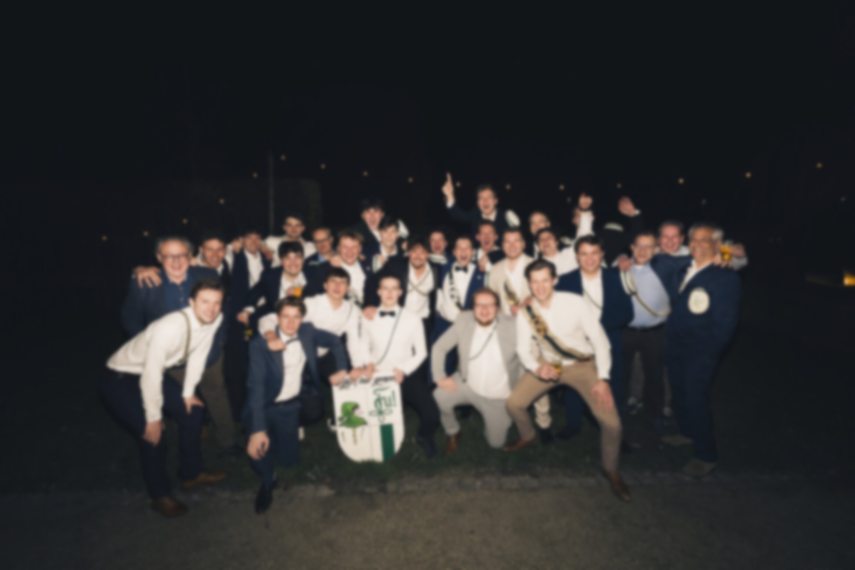 Groepsfoto van leden en oud-leden van Tyl Uylenspiegel met het clubschild